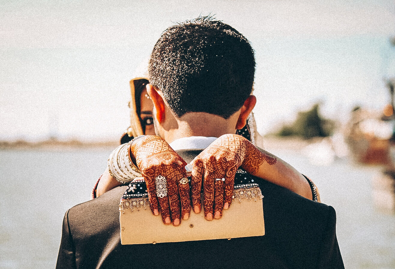 Couple embracing, mehndi-covered hands on groom's shoulder